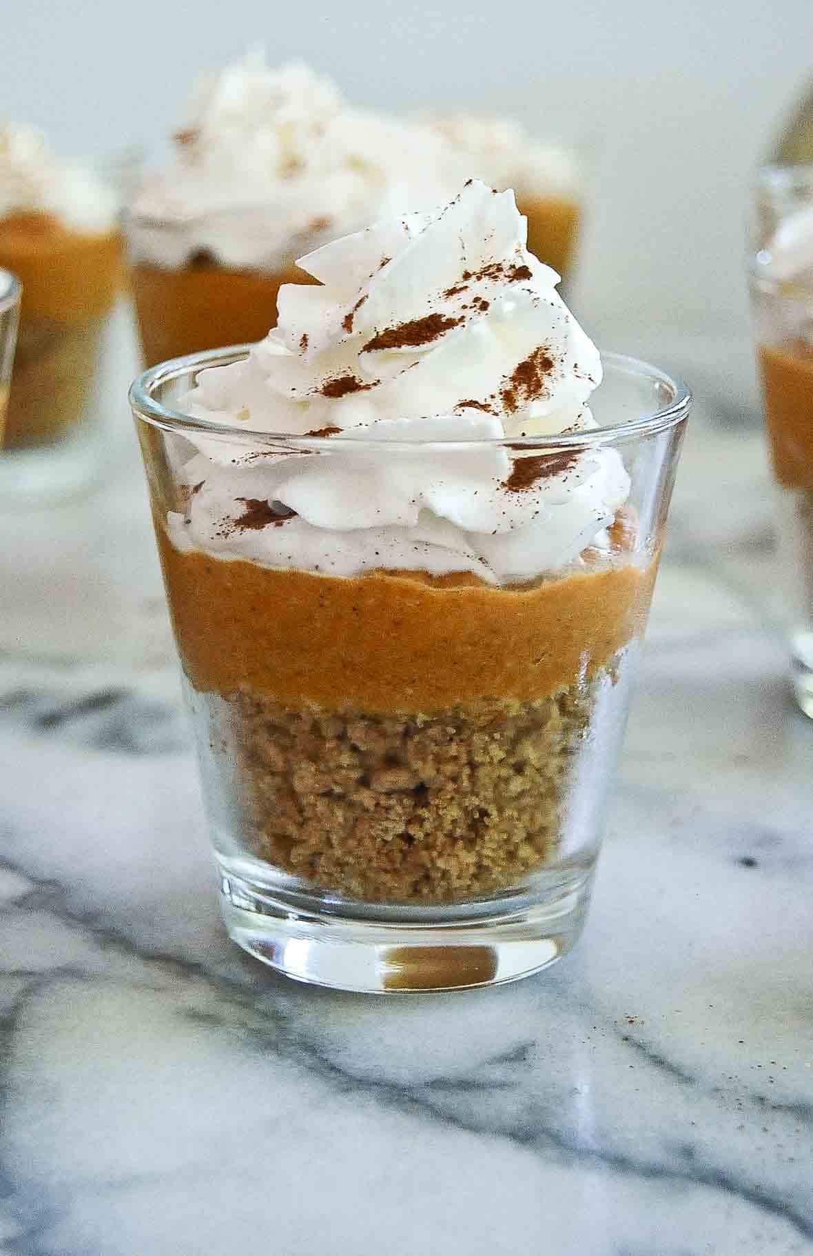 side view of pumpkin pie in a cup with whipped cream and cinnamon on top.