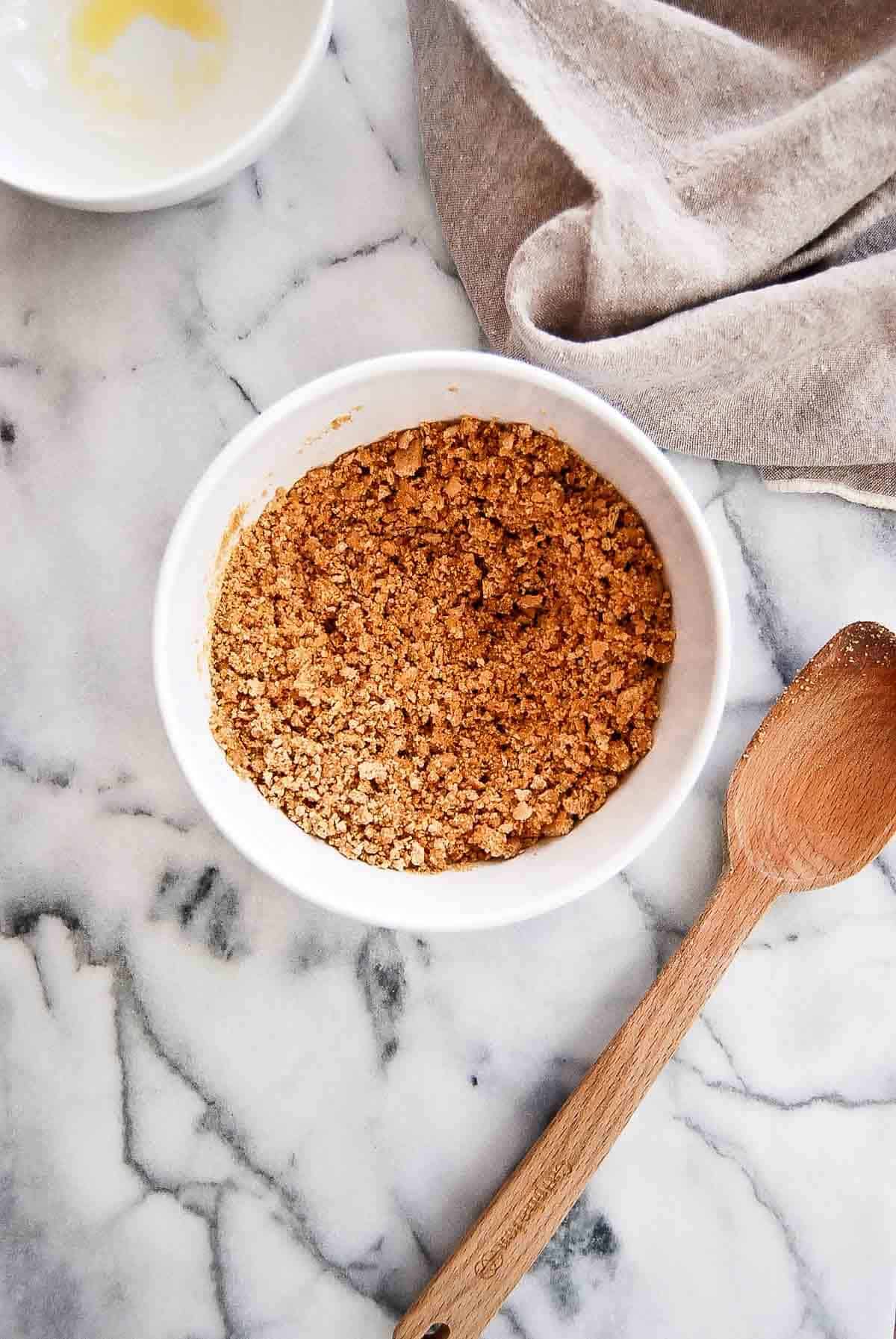 crumbled graham cracker mixed with melted butter in bowl on countertop.