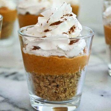 side view of pumpkin pie in a cup with graham cracker crust, pumpkin pie filling and whipped cream on top.