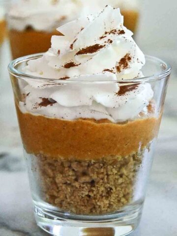 side view of pumpkin pie in a cup with graham cracker crust, pumpkin pie filling and whipped cream on top.