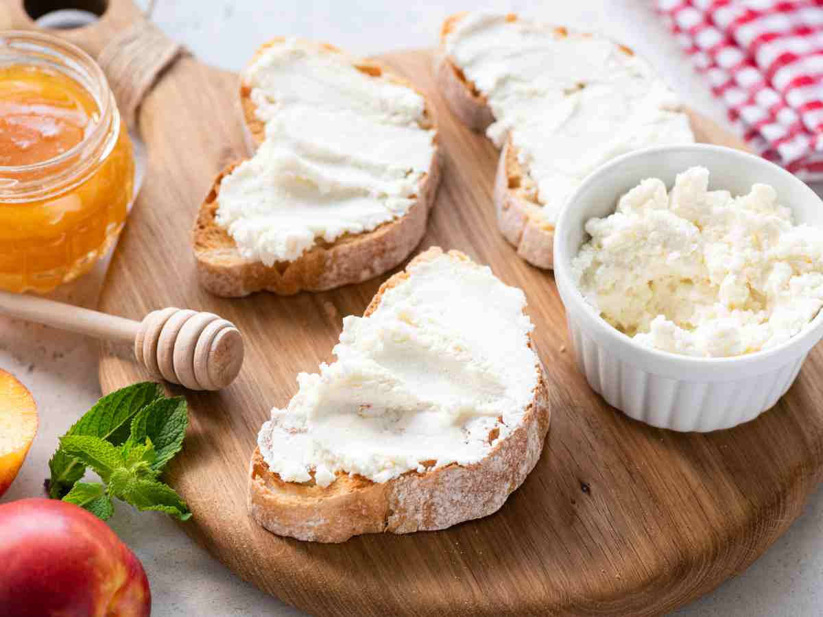 crusty bread with ricotta cheese spread on top on a cutting board.
