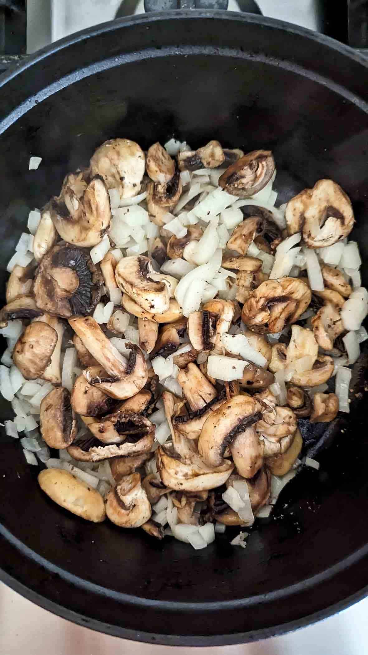 mushrooms and onions in a dutch oven on the stove.