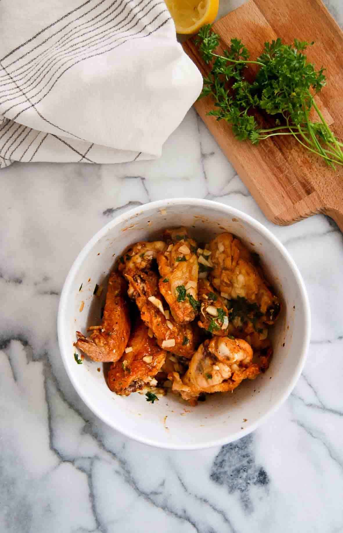 partially baked chicken wings in bowl with garlic sauce.