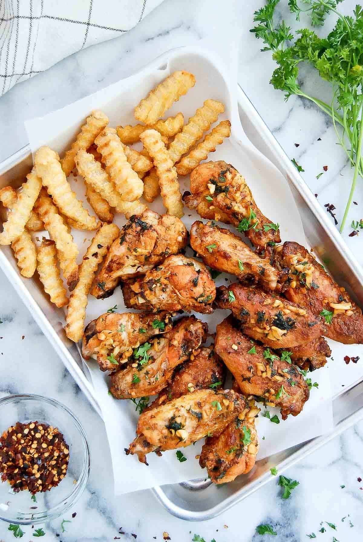 spanish style chicken wings with fries on tray.