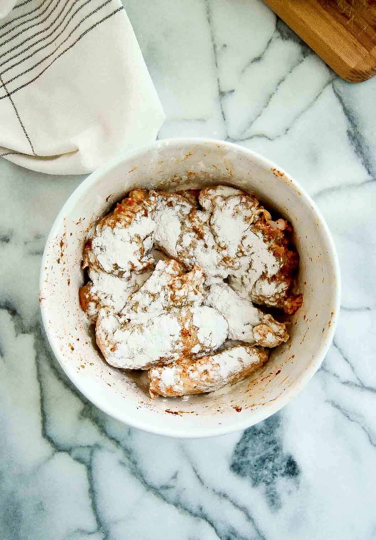 marinated chicken wings tossed with baking powder in bowl.