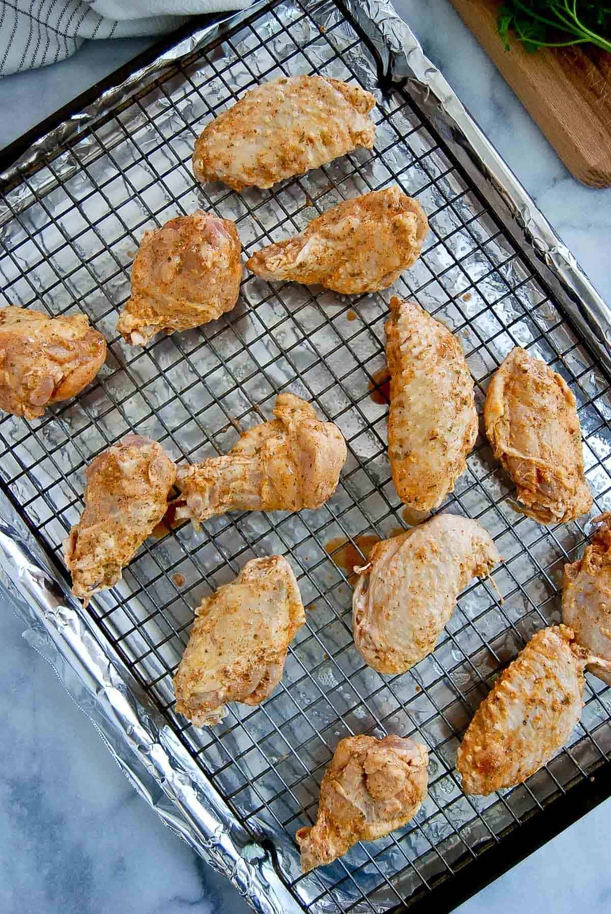 baking powder dusted chicken wings on wire rack set atop a baking tray lined with foil.