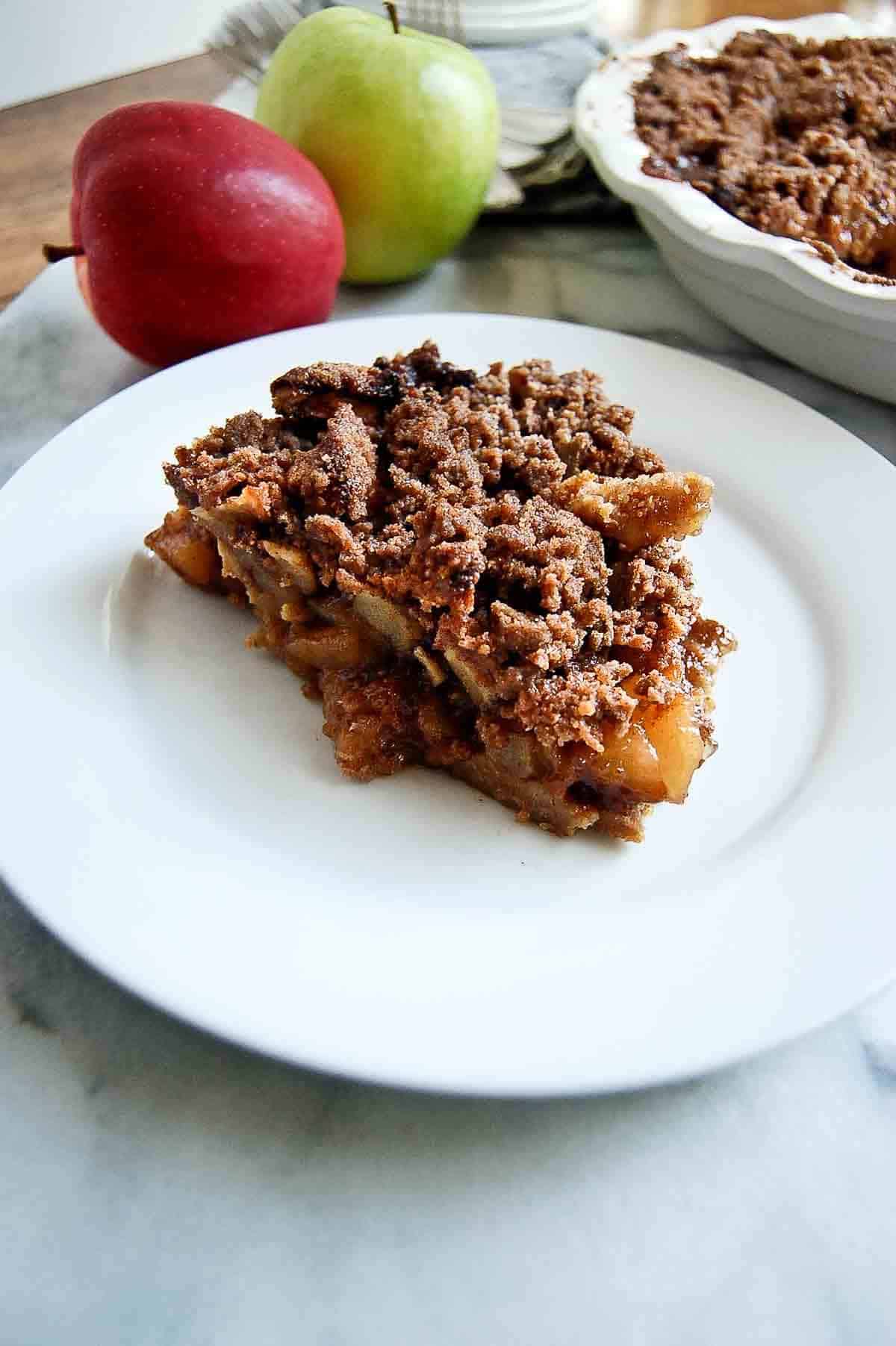 slice of baked dutch apple pie with a graham cracker crust on plate.