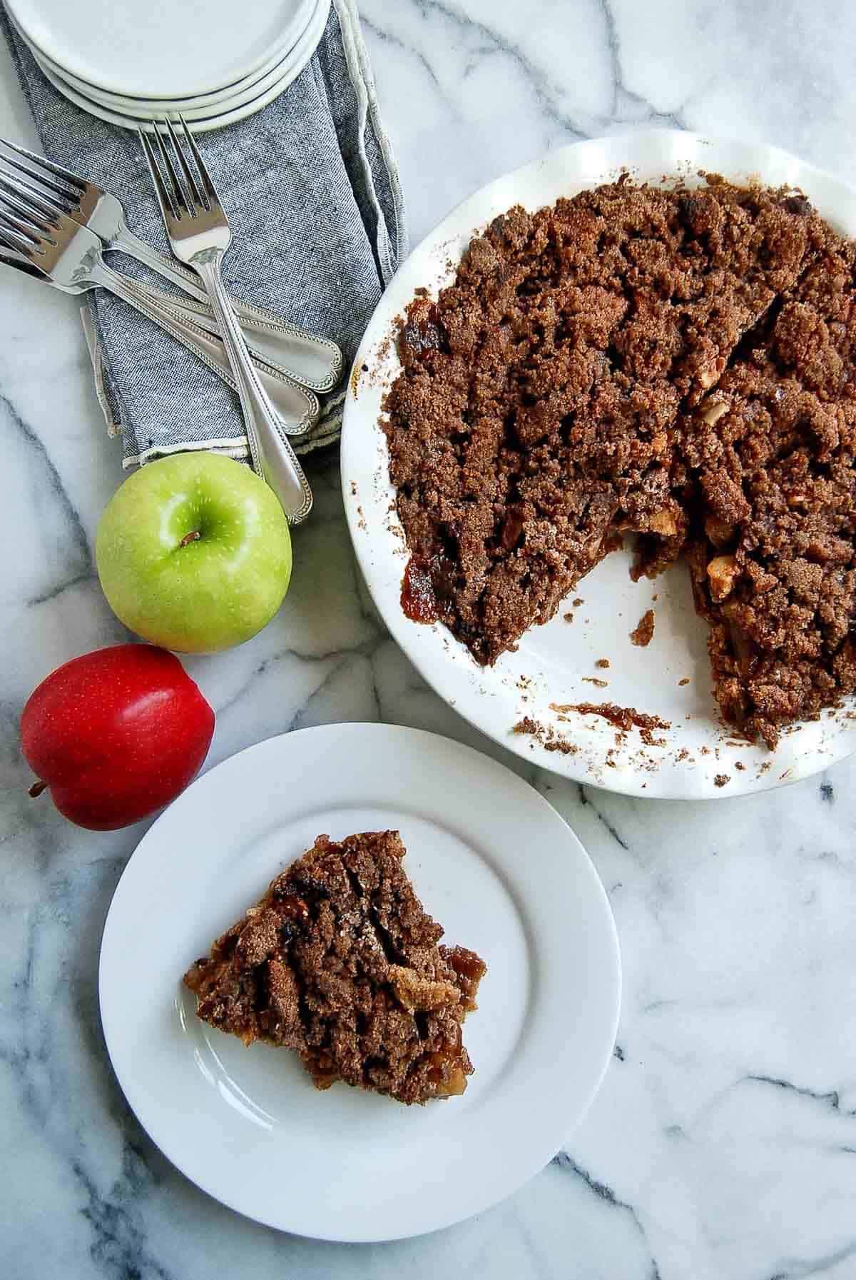 slice of baked dutch apple pie with a graham cracker crust on plate with full pie next to it.