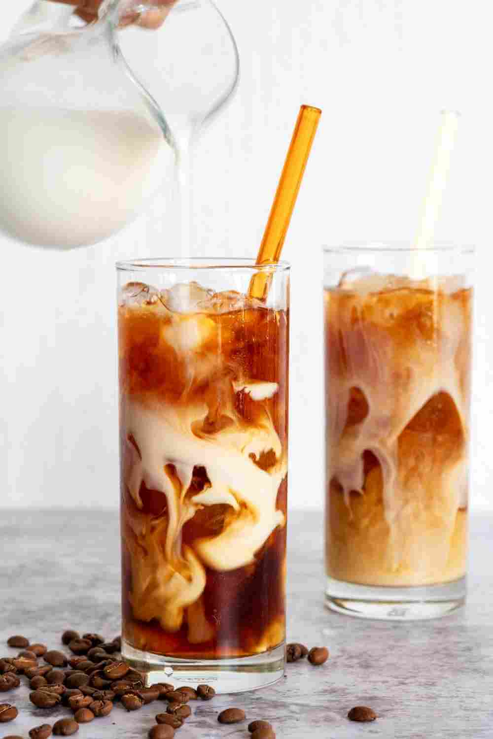 cold brew coffee in cups with cream being poured into the cups.