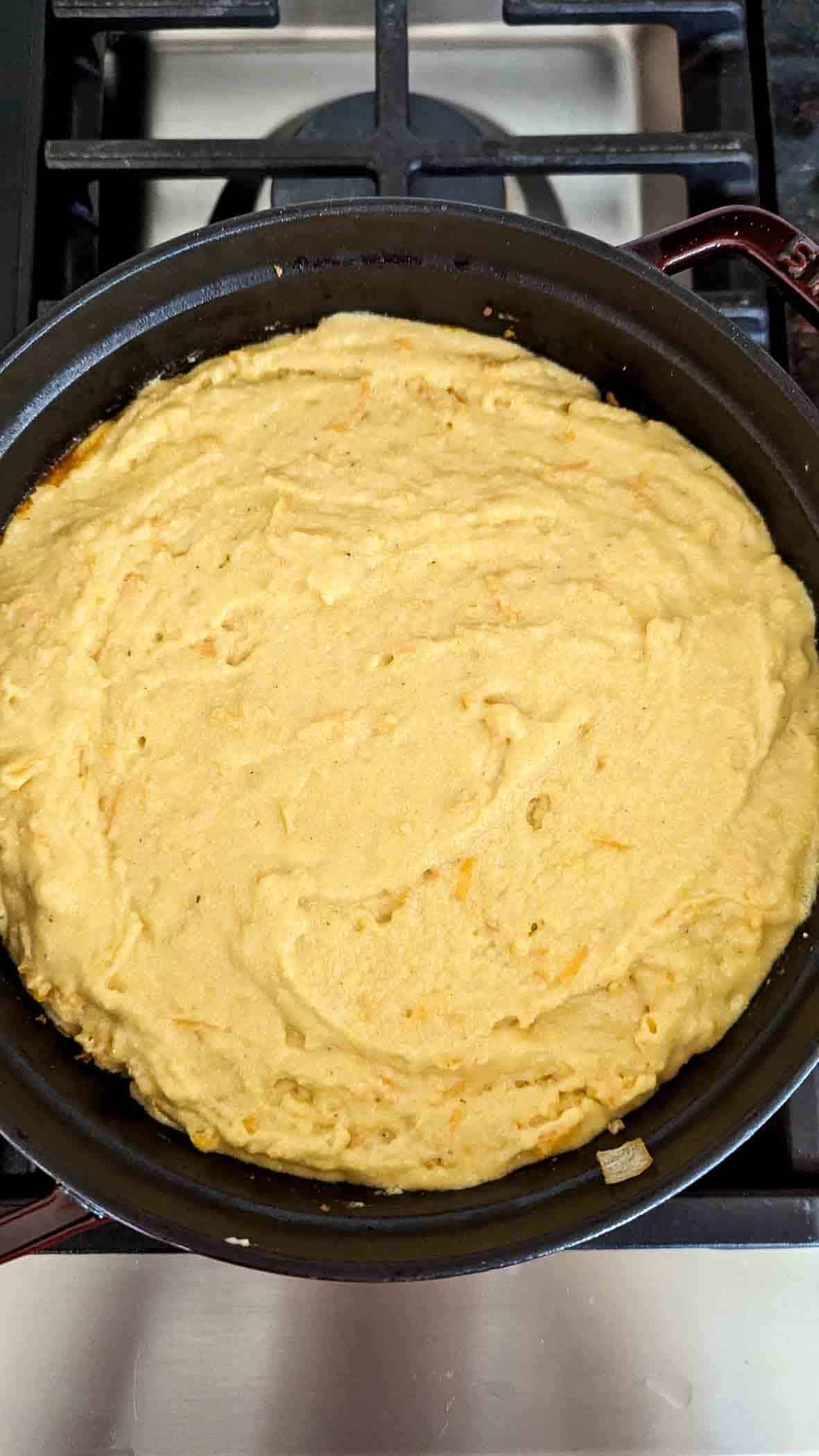 ground beef mixture with cornbread batter topping in dutch oven on stovetop.