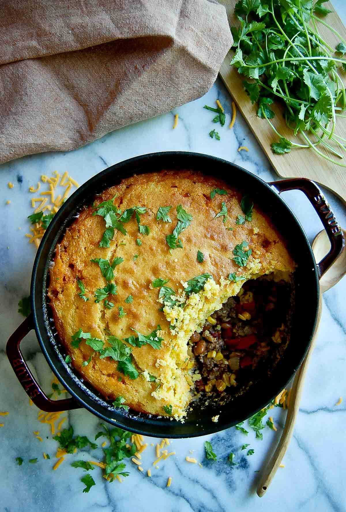 cornbread cowboy casserole in dutch oven on countertop with section of casserole spooned out.