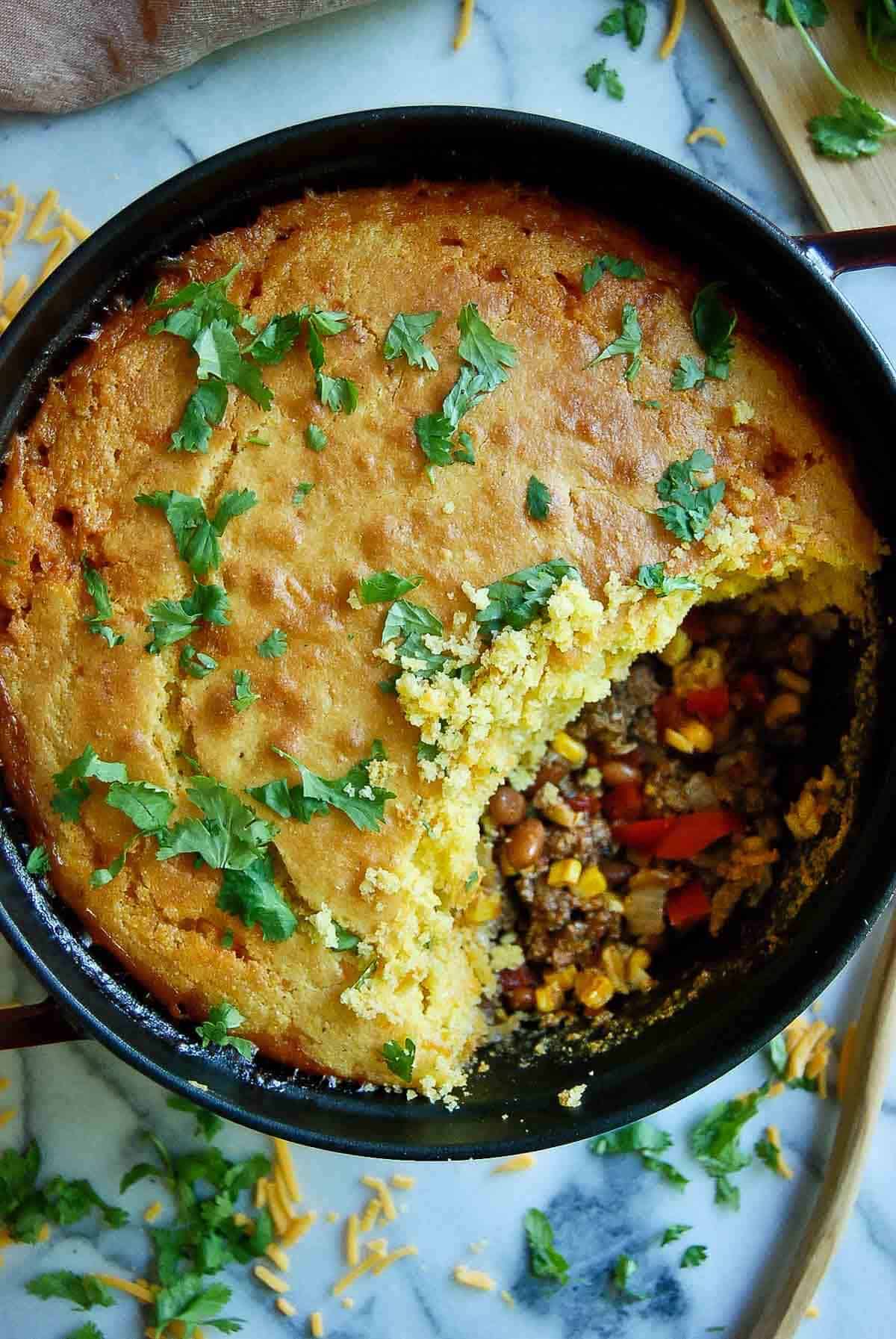 cornbread cowboy casserole in dutch oven on countertop with section of casserole spooned out.