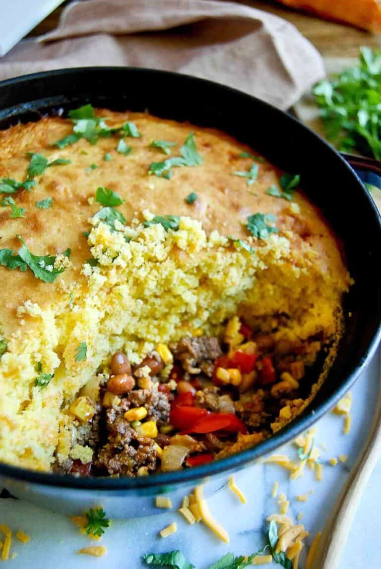 cornbread cowboy casserole in dutch oven on countertop with section of casserole spooned out.
