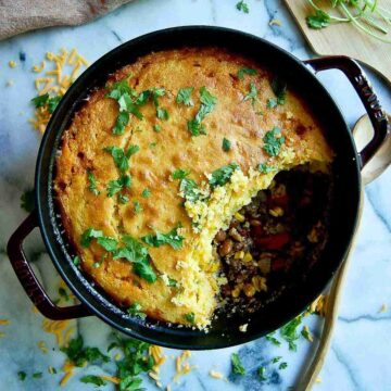 cornbread cowboy casserole in dutch oven on countertop with section of casserole spooned out.