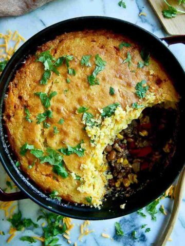 cornbread cowboy casserole in dutch oven on countertop with section of casserole spooned out.