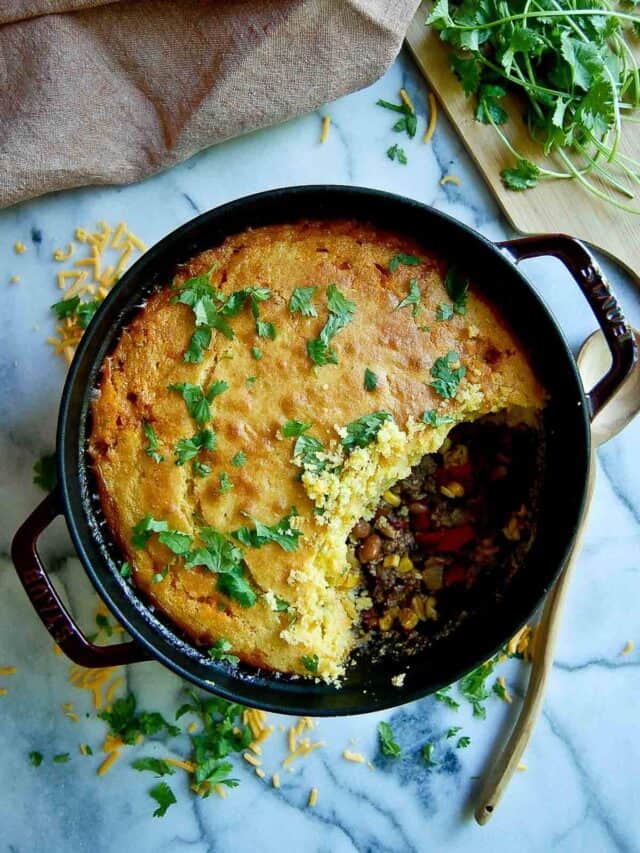 cornbread cowboy casserole in dutch oven on countertop with section of casserole spooned out.