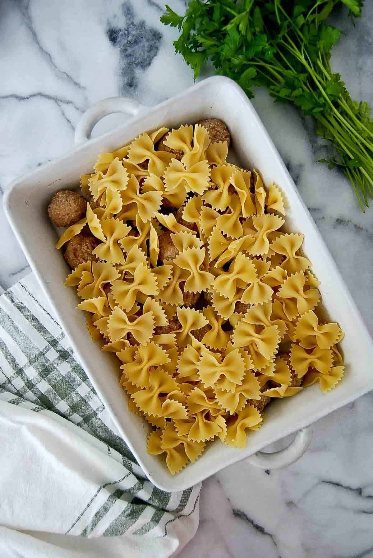 meatballs and uncooked pasta in baking dish.