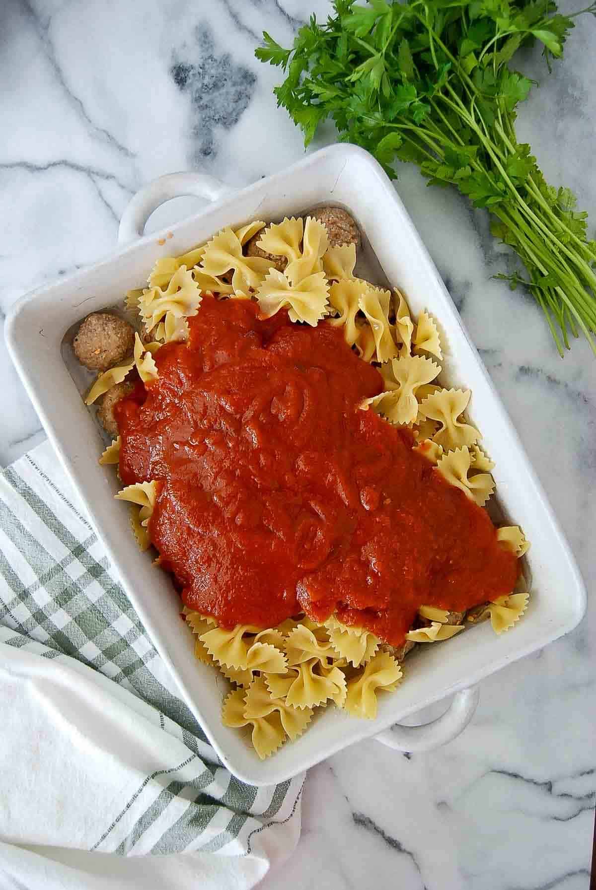 meatballs, uncooked pasta and pasta sauce in baking dish on countertop.