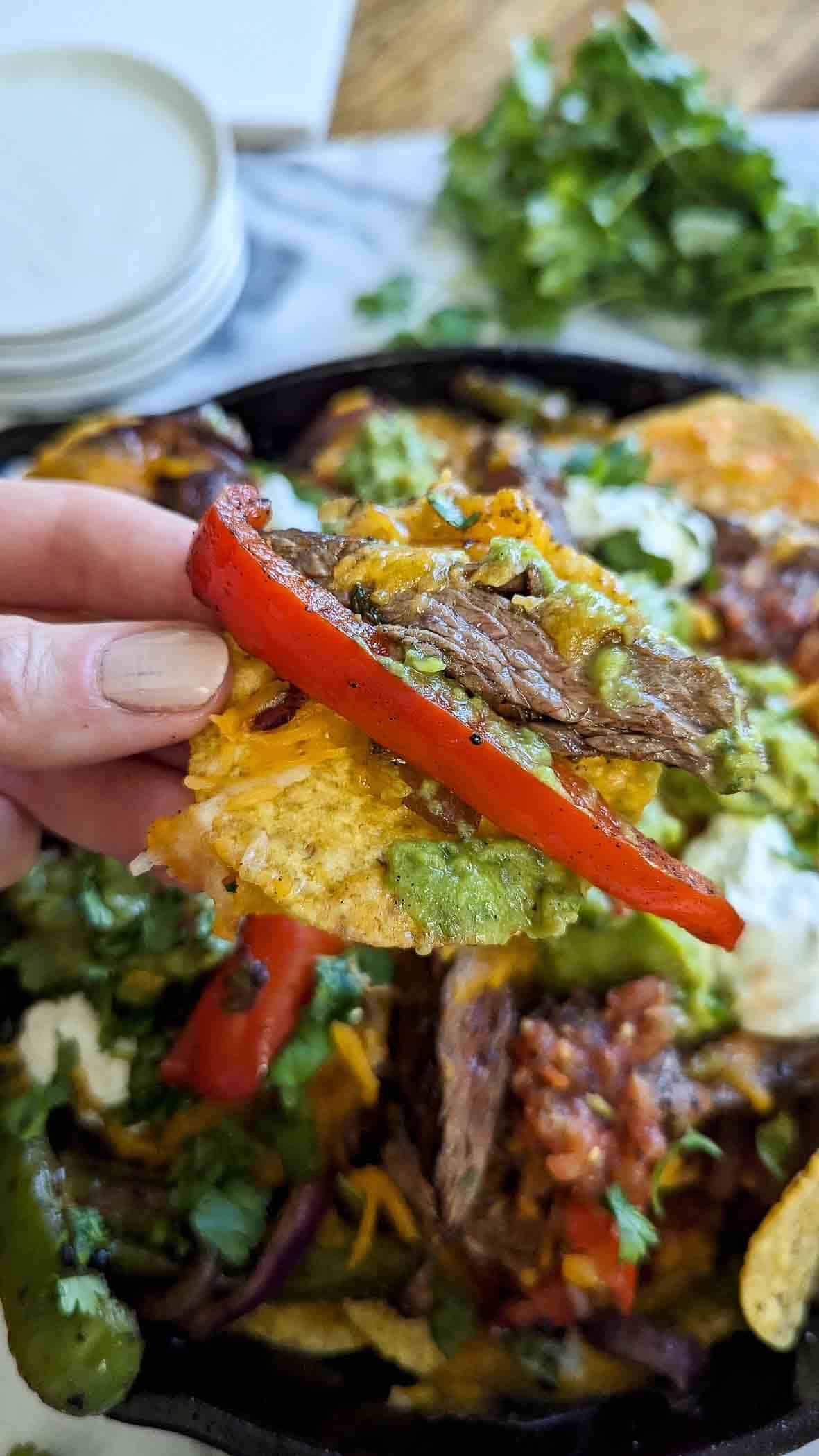 hand holding a chip with skirt steak fajita nachos.