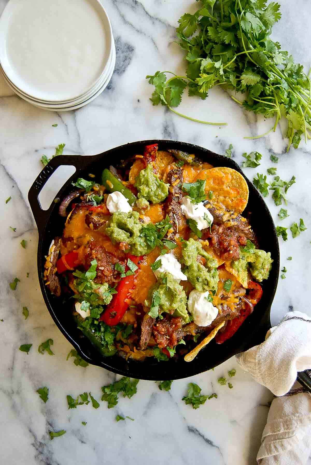 loaded steak fajita nachos in skillet with sour cream, guacamole and salsa.