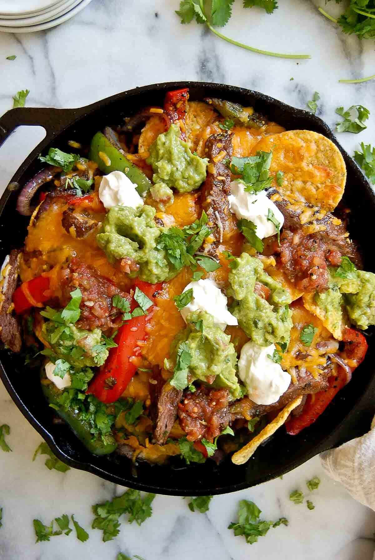 loaded steak fajita nachos in skillet with sour cream, guacamole and salsa.