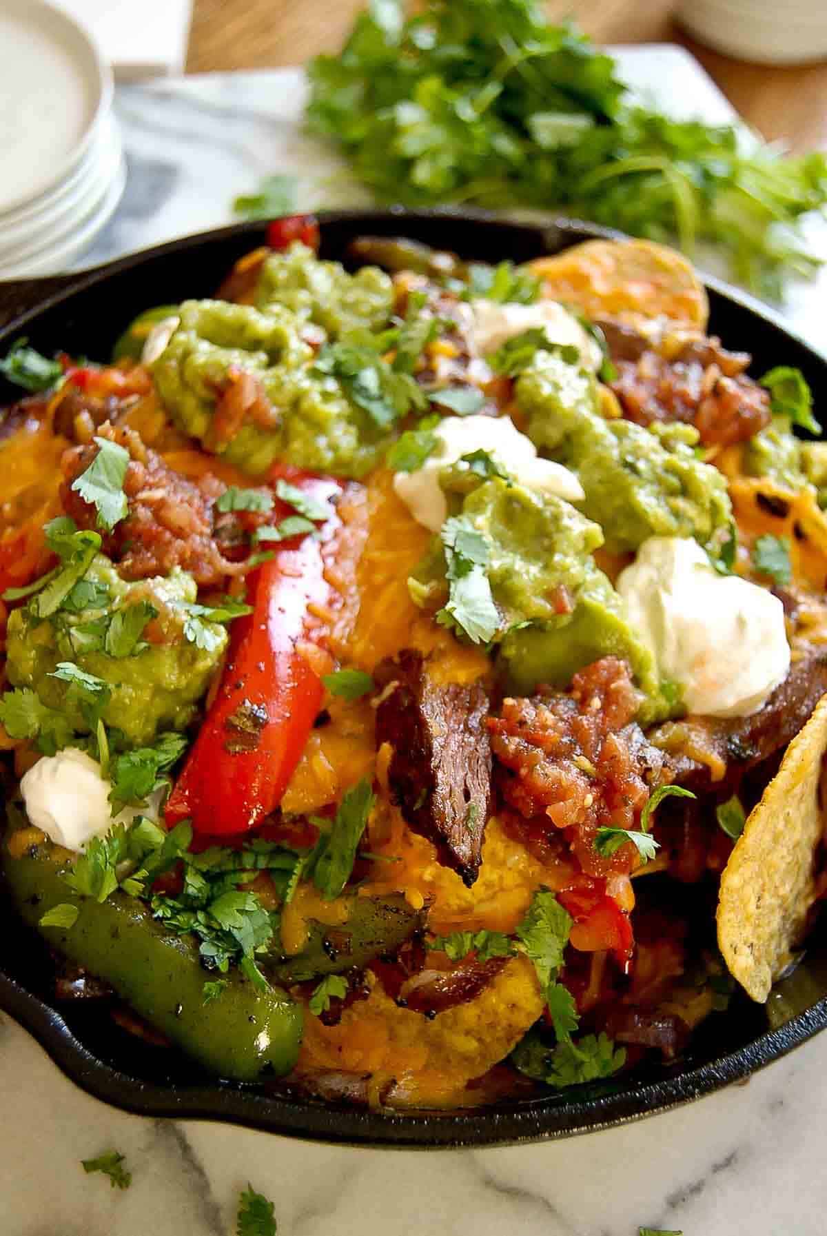 closeup side view of steak fajita nachos in skillet.