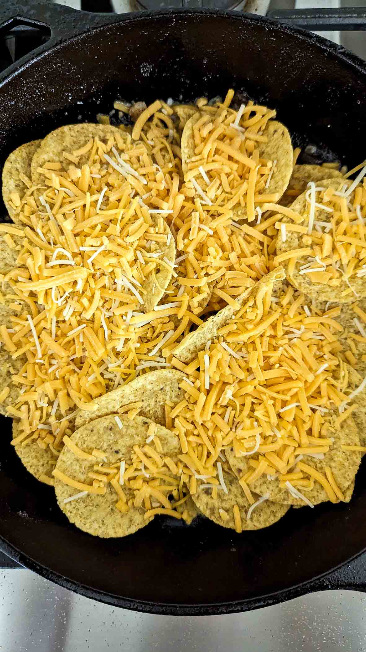 corn tortilla chips in skillet topped with shredded cheddar cheese.