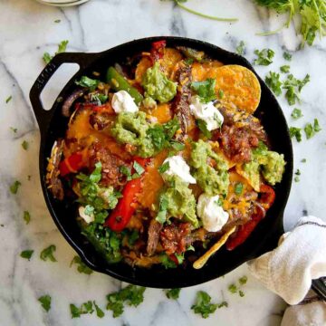 skirt steak fajita nachos in skillet with guacamole, sour cream and salsa on top.