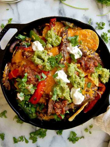 skirt steak fajita nachos in skillet with guacamole, sour cream and salsa on top.