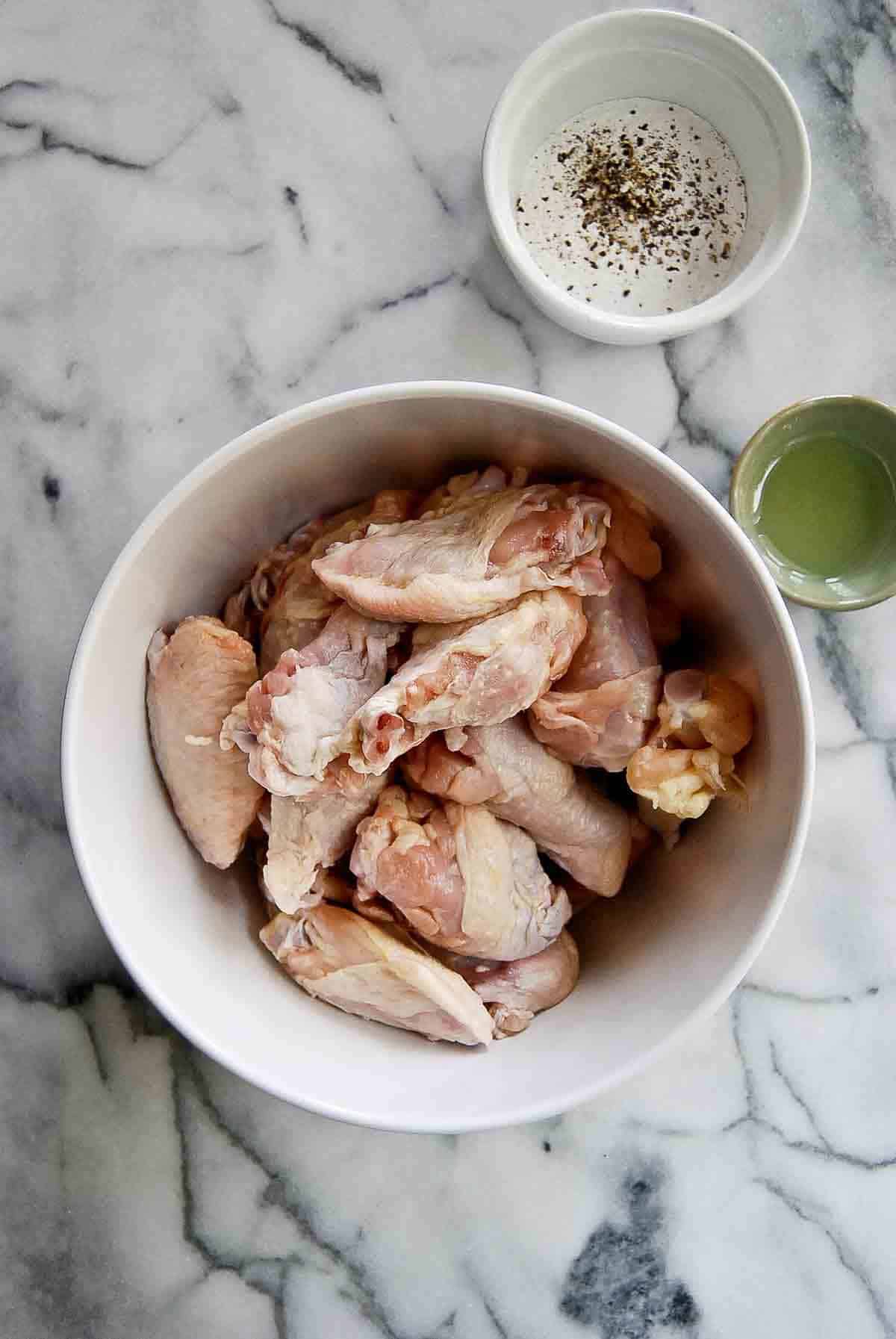 raw chicken wings in bowl with baking powder mix next to it.