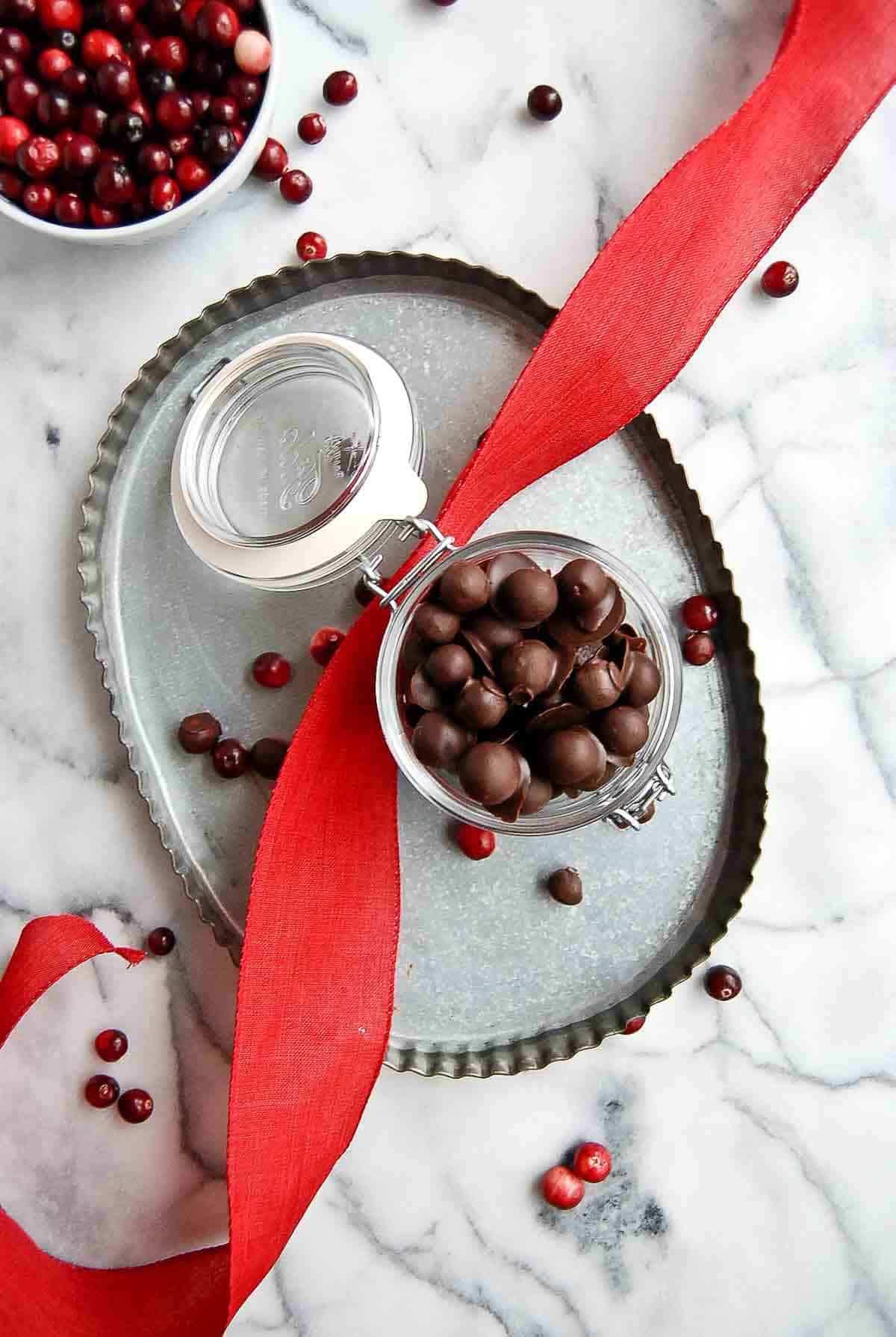 jar of chocolate covered cranberries on tray with red ribbon draped across it.