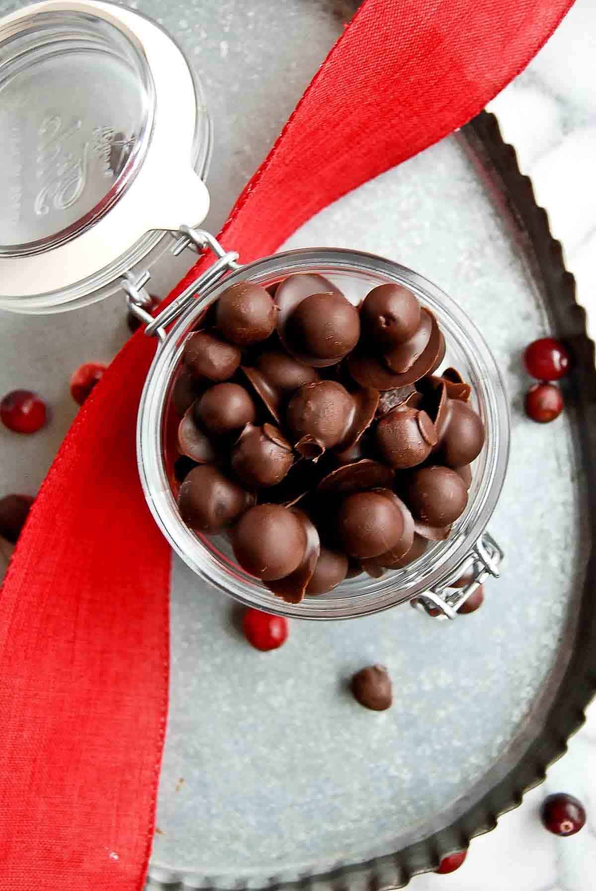 jar of chocolate covered cranberries on tray with red ribbon draped across it.