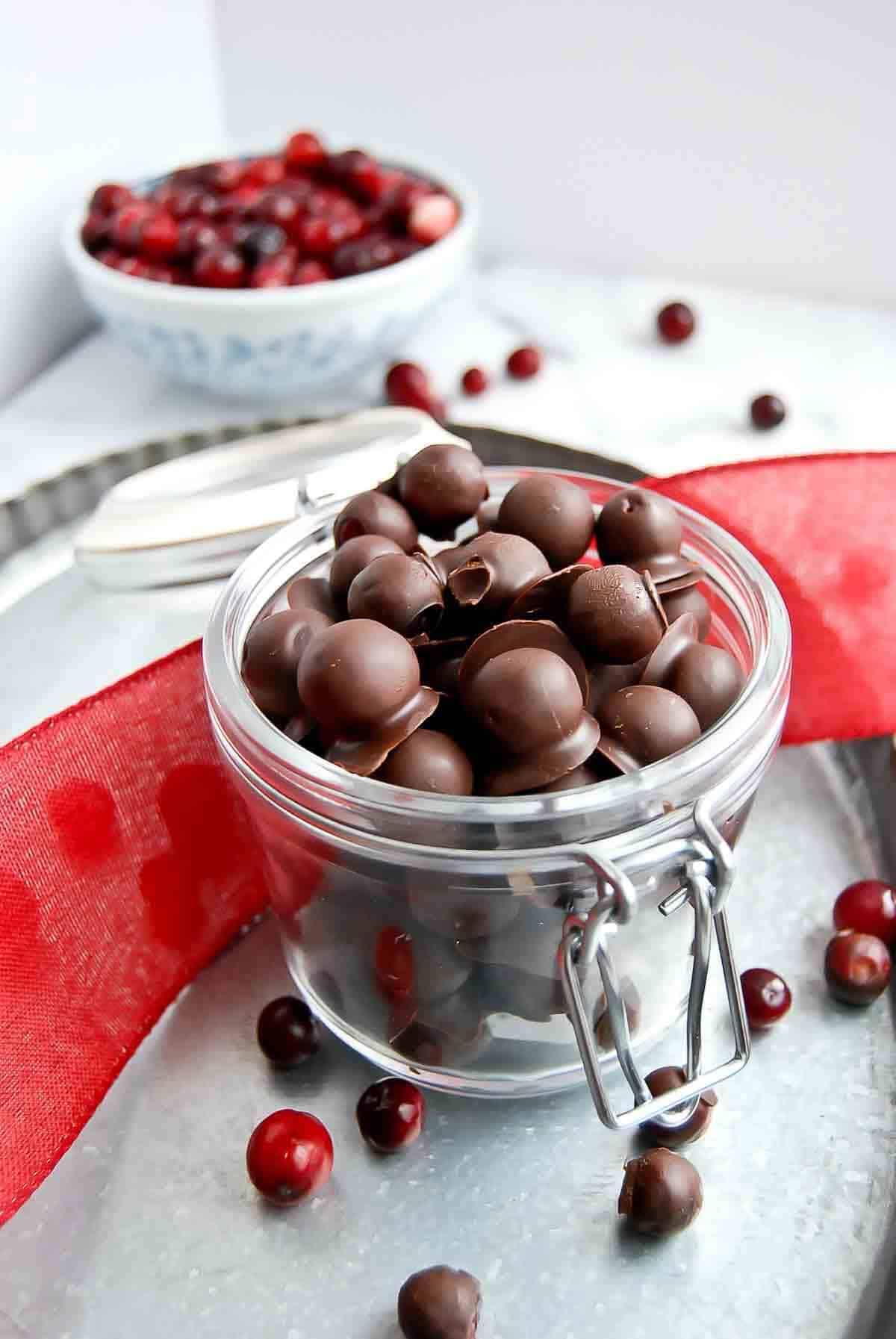 jar of chocolate covered cranberries on tray with red ribbon draped across it.