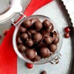 jar of chocolate covered cranberries on tray with red ribbon draped across it.