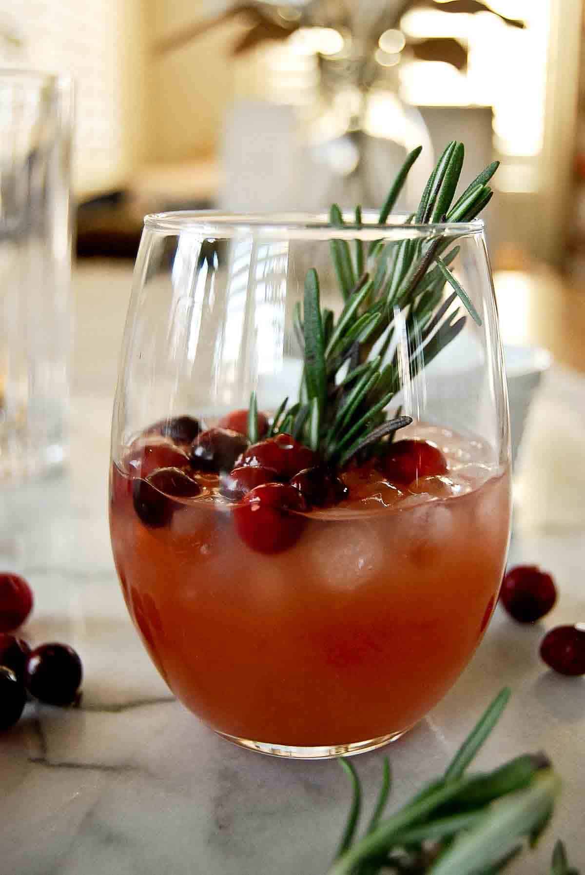 side view of cranberry orange whiskey sour with fresh rosemary and cranberry garnish.