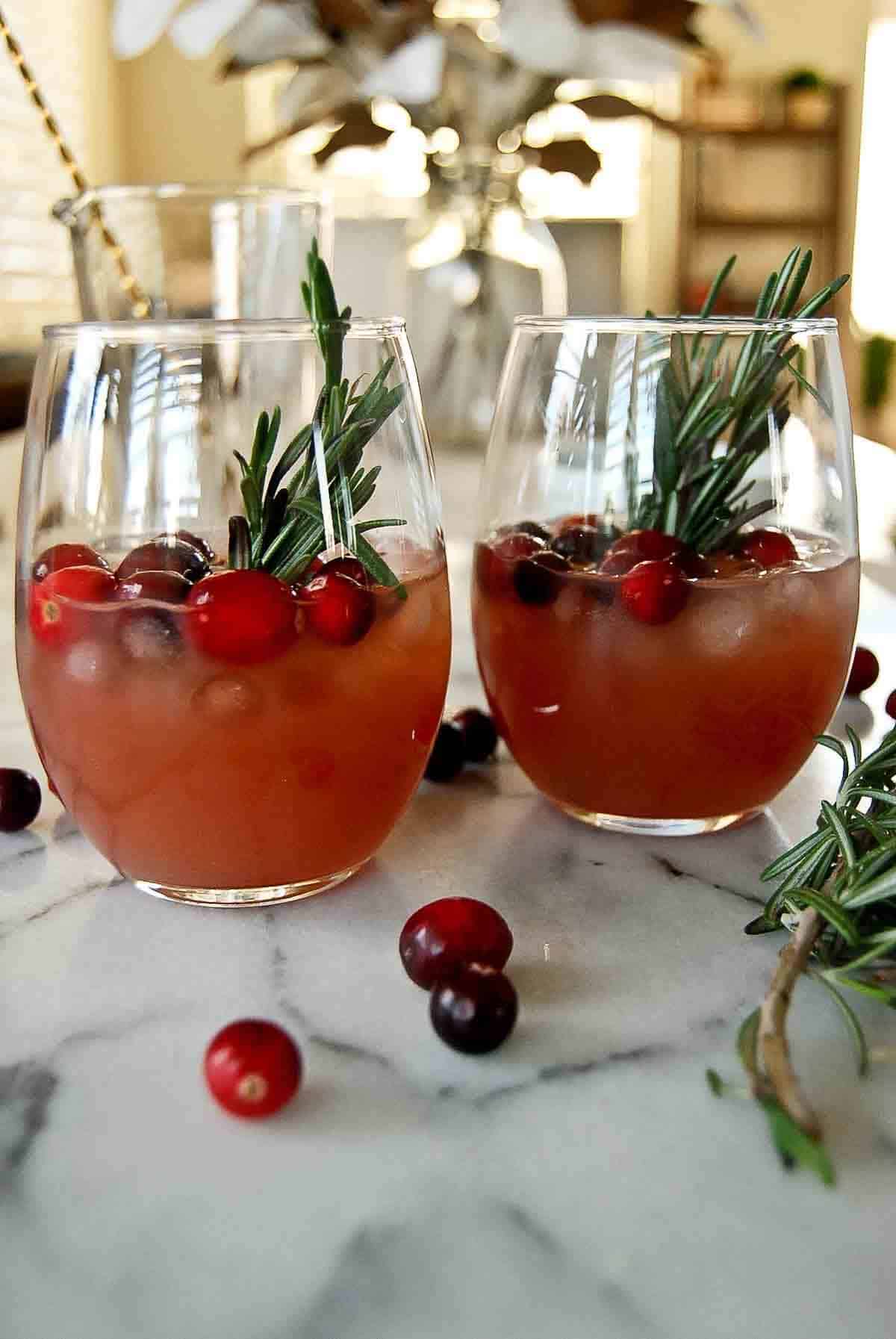 side view of cranberry orange whiskey sours with fresh rosemary and cranberry garnish.