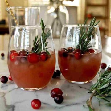 side view of cranberry orange whiskey sours with fresh rosemary and cranberry garnish.
