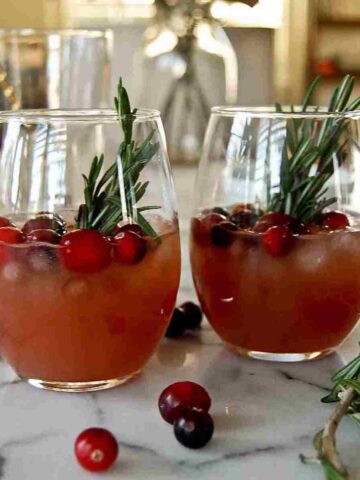 side view of cranberry orange whiskey sours with fresh rosemary and cranberry garnish.