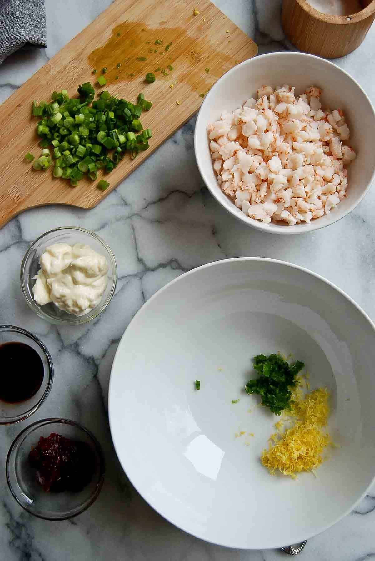 spicy shrimp salad ingredients on countertop with lemon zest and grated jalapeno in bowl.