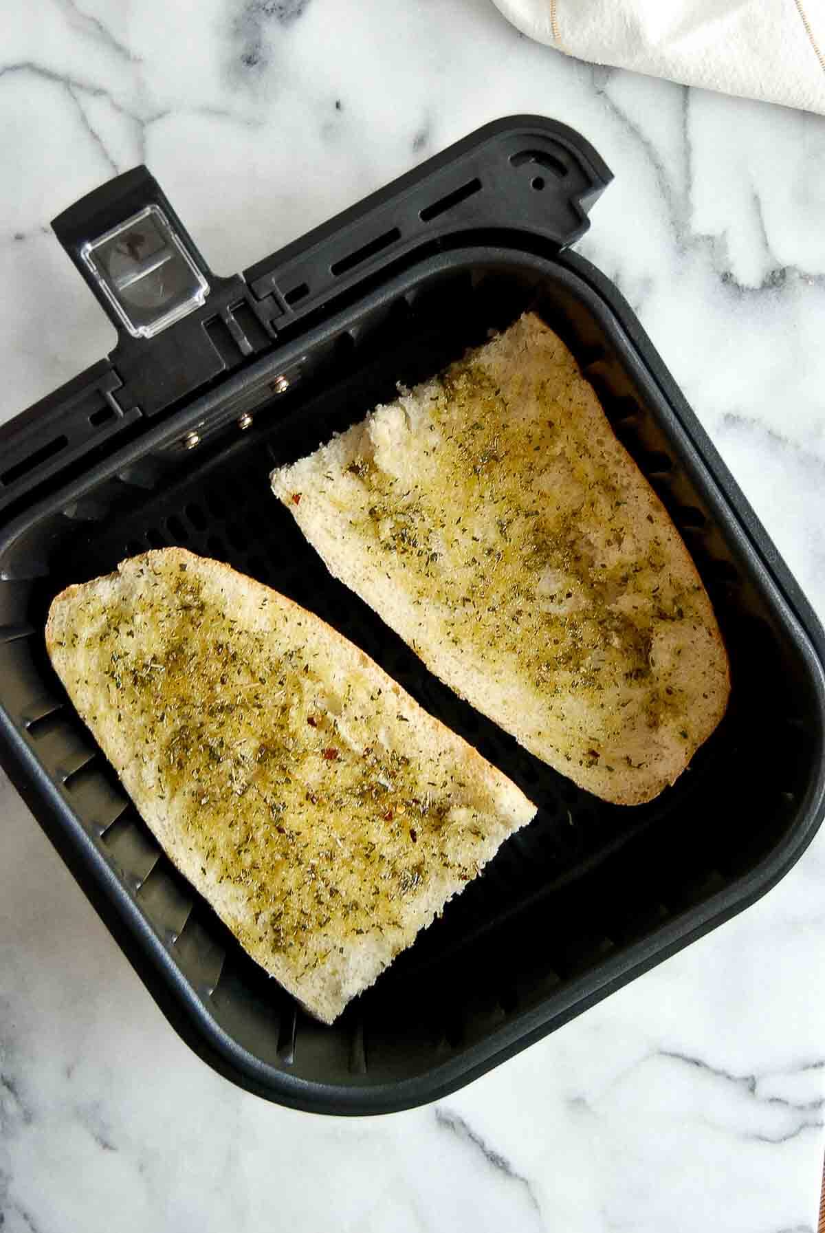 french bread halves with oil and Italian seasoning brushed onto the top, in air fryer basket.