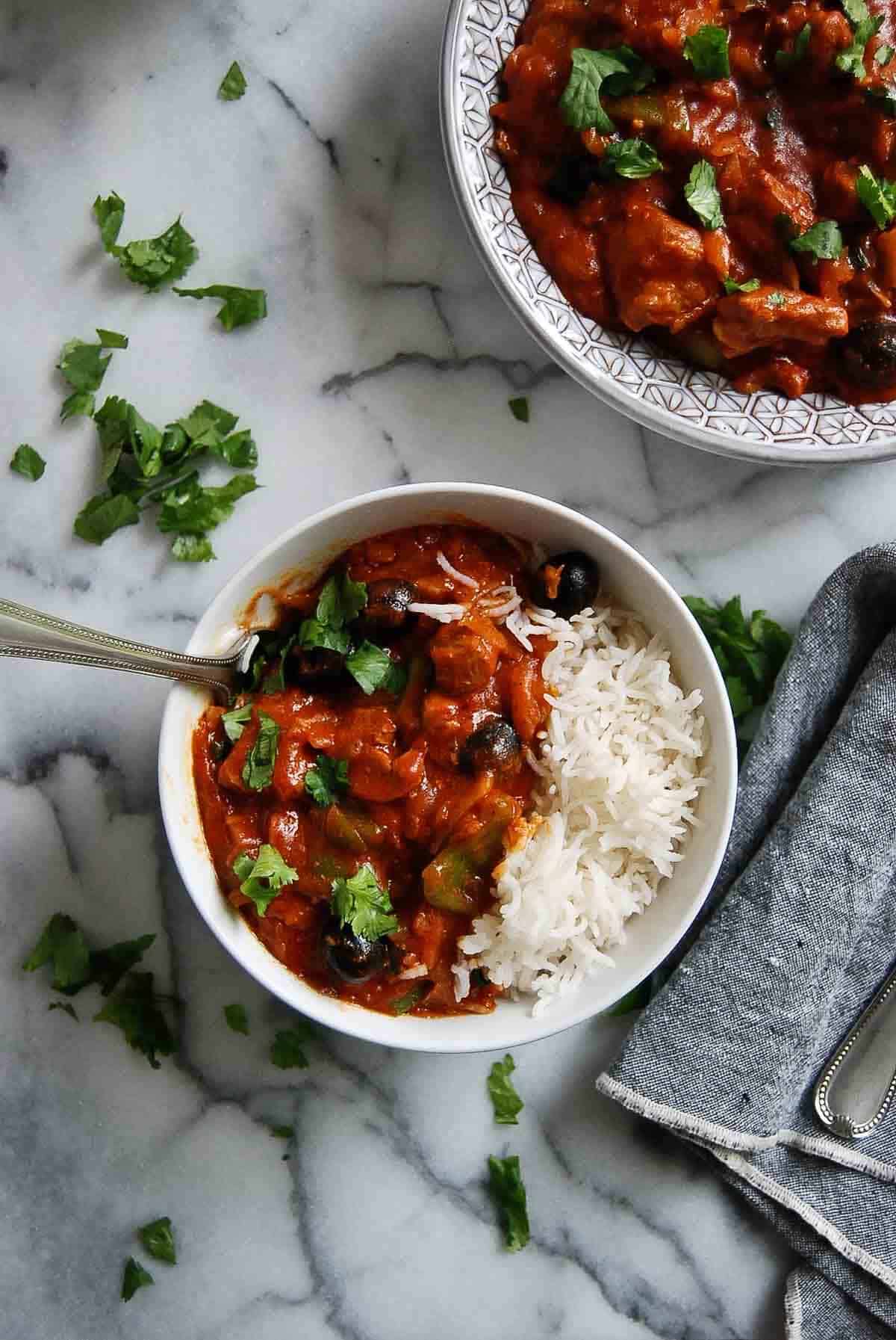 pastele stew in serving bowl, with rice to the side and 1 serving dished out on countertop.