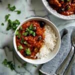 pastele stew in serving bowl, with rice to the side and 1 serving dished out on countertop.