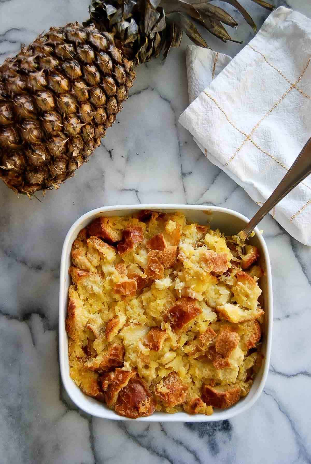 scalloped pineapple in baking dish with spoon.