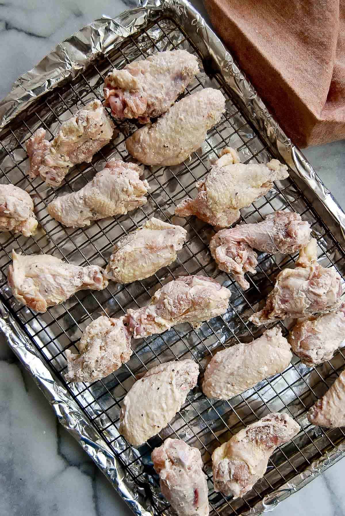 chicken wings on pan lined with foil and toped with a rack.