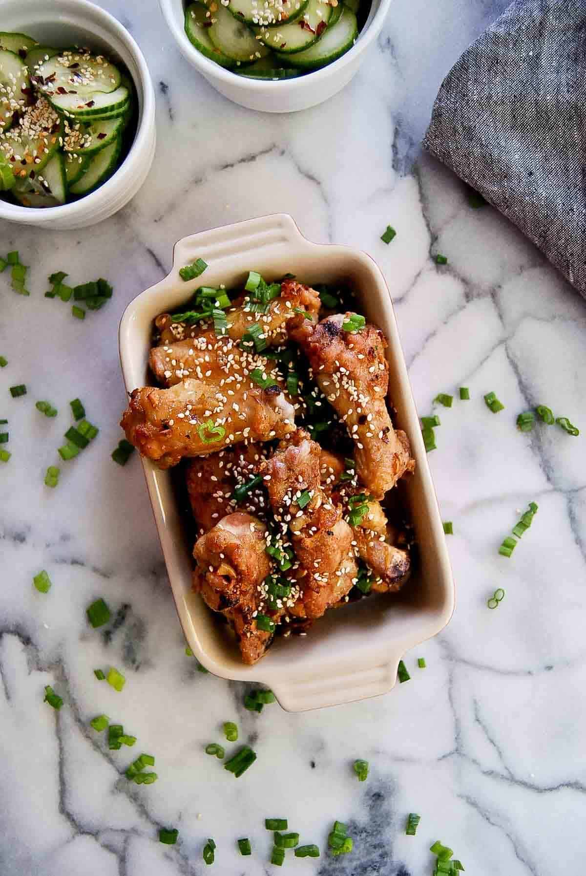 soy garlic chicken wings in serving dish with cucumber salad on the side.