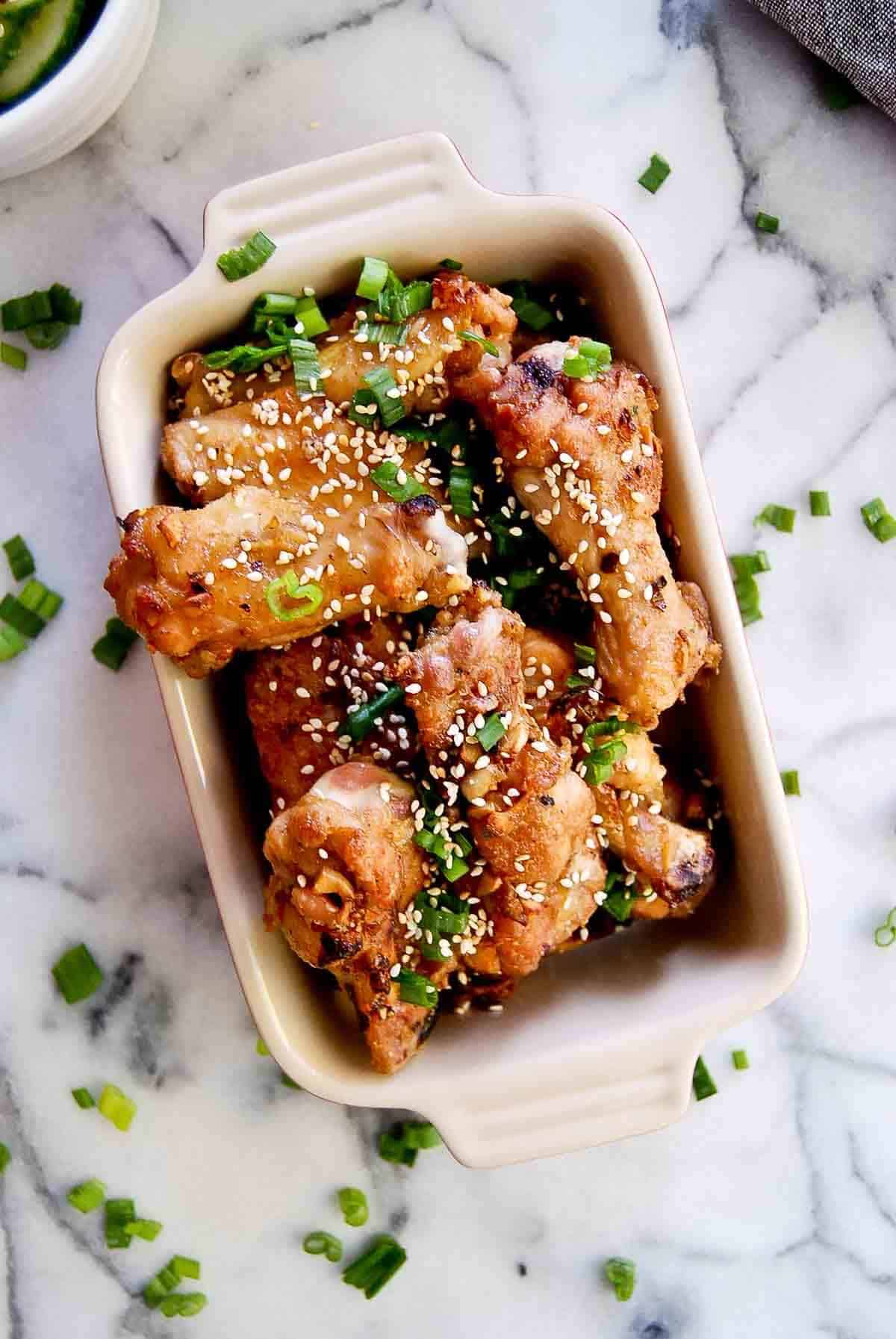 closeup of soy garlic chicken wings in serving dish with scallions and sesame seeds on top.