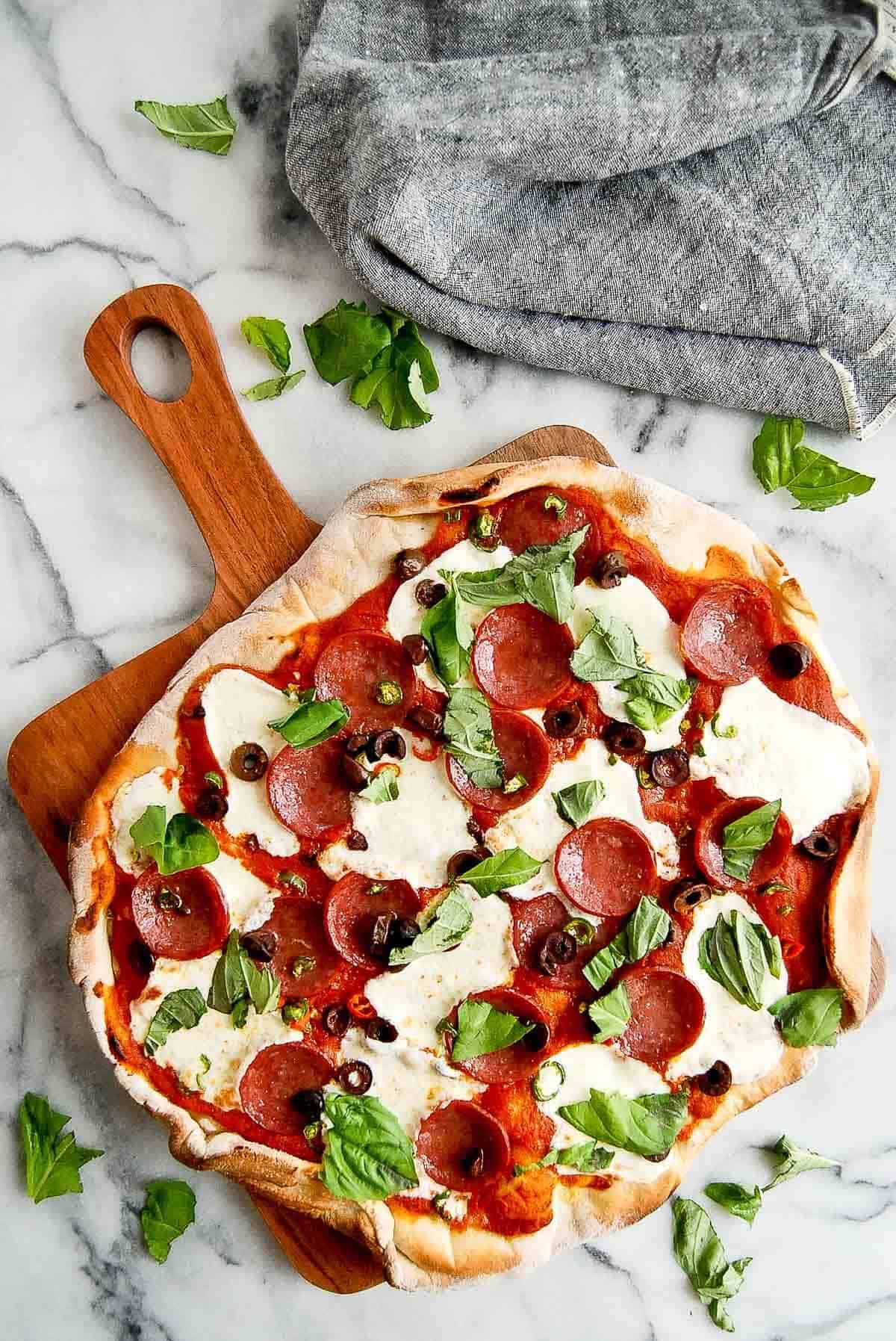 spicy diavola pizza with hot salami on cutting board, with basil on top.