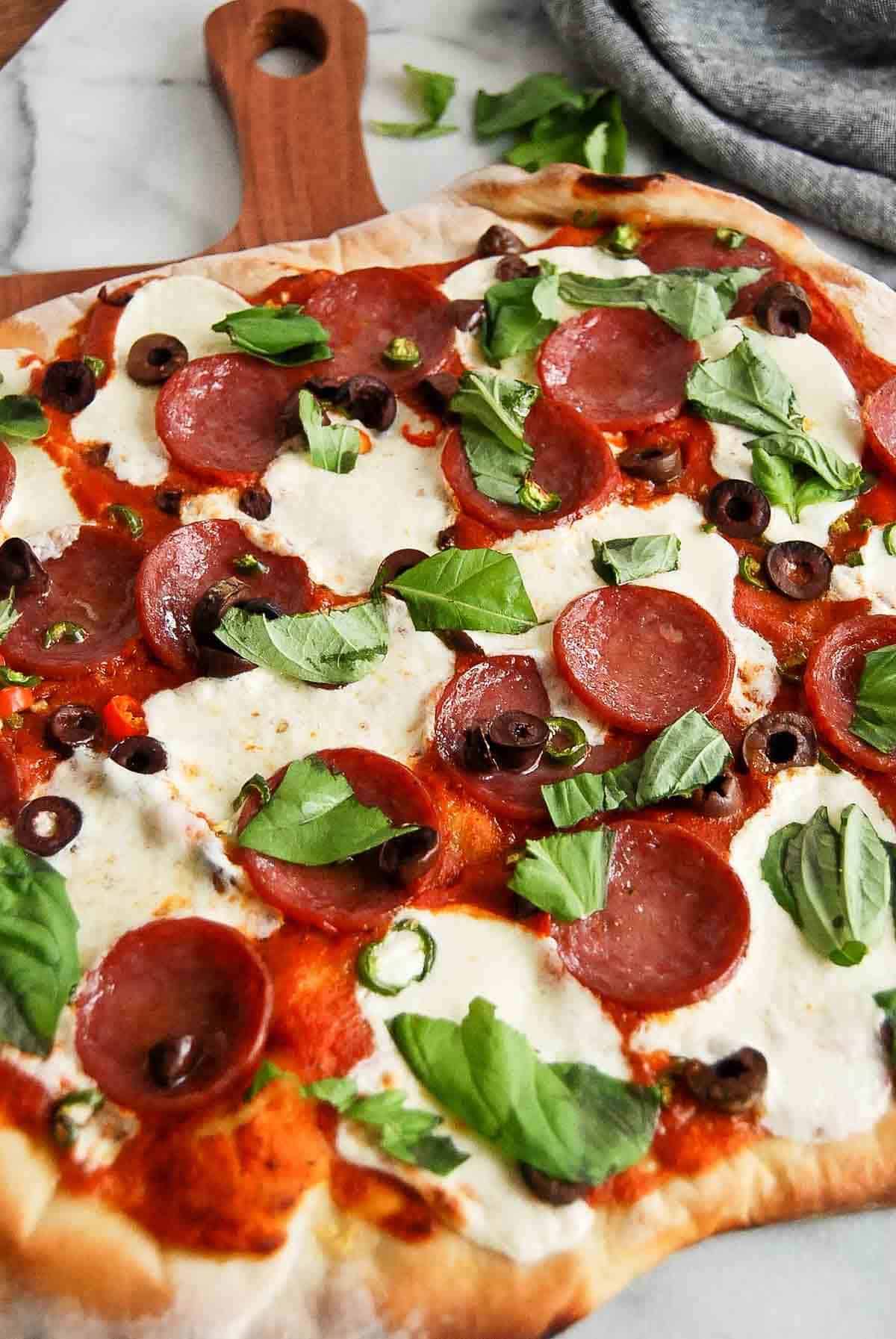 side view of spicy diavola pizza with hot salami on cutting board, with basil on top.