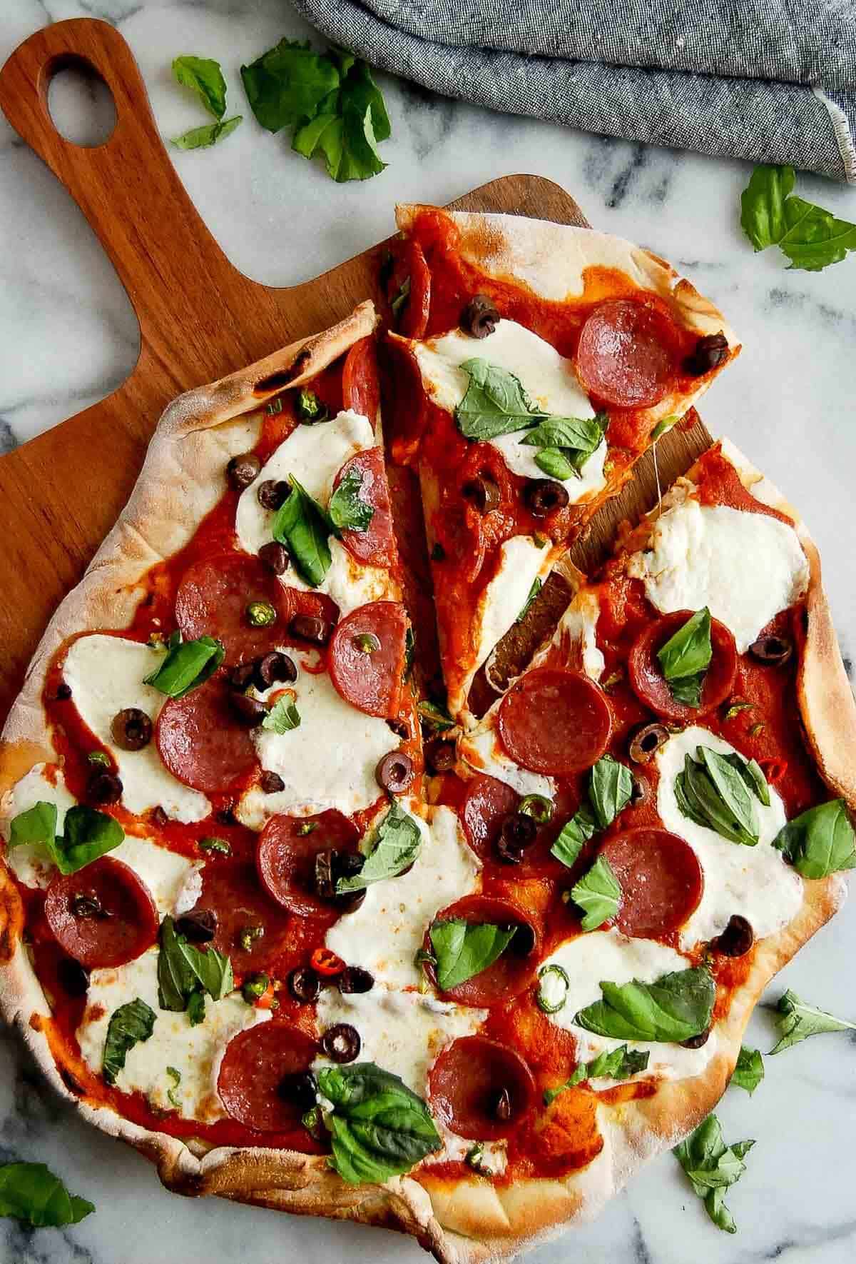 spicy diavola pizza with hot salami on cutting board, with basil on top, one slice cut out.