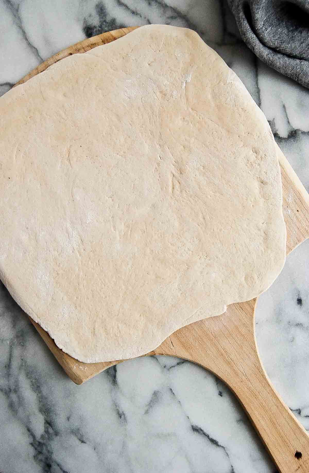 pizza dough rolled out onto pizza peel.